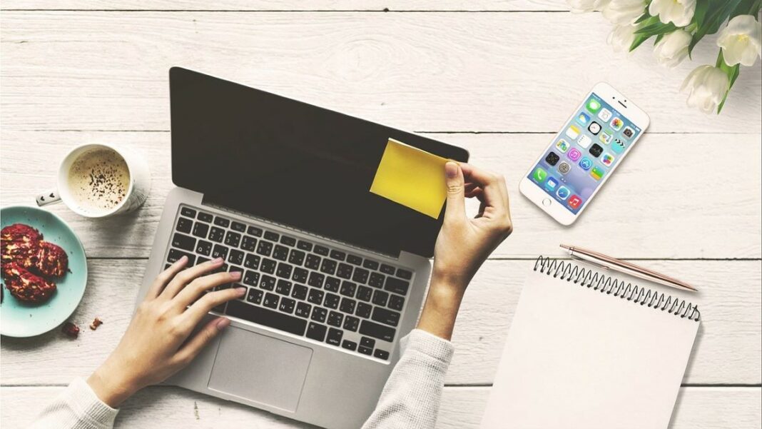 managing finances for a home-based business represented by a woman's hands resting on an open laptop on a wooden table that has been painted white