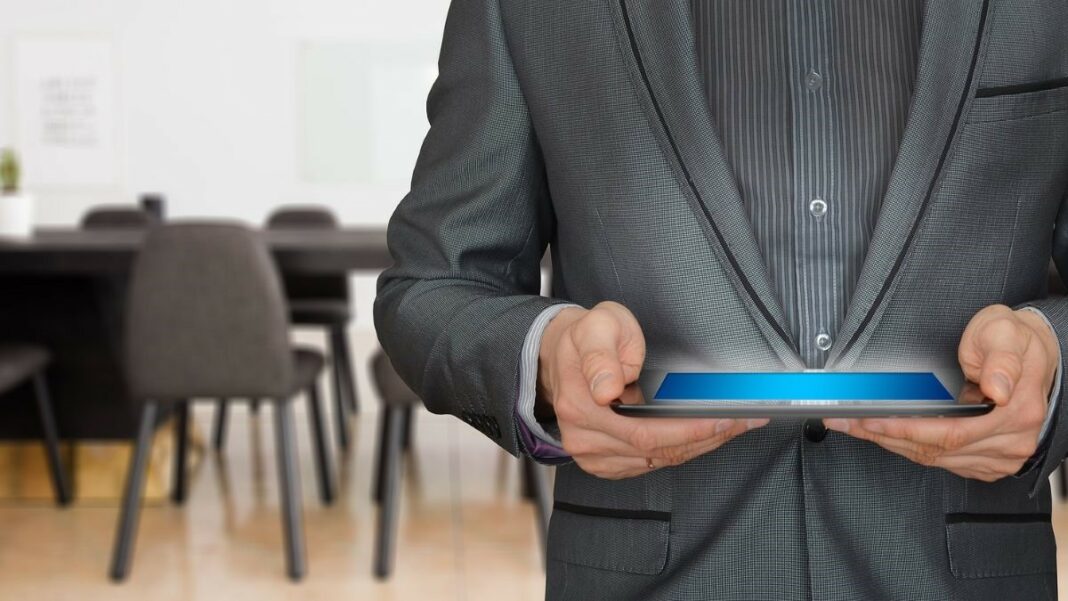 sales operations represented by well-dressed businessman holding a tablet in a conference room, standing in front of a black table and several chairs