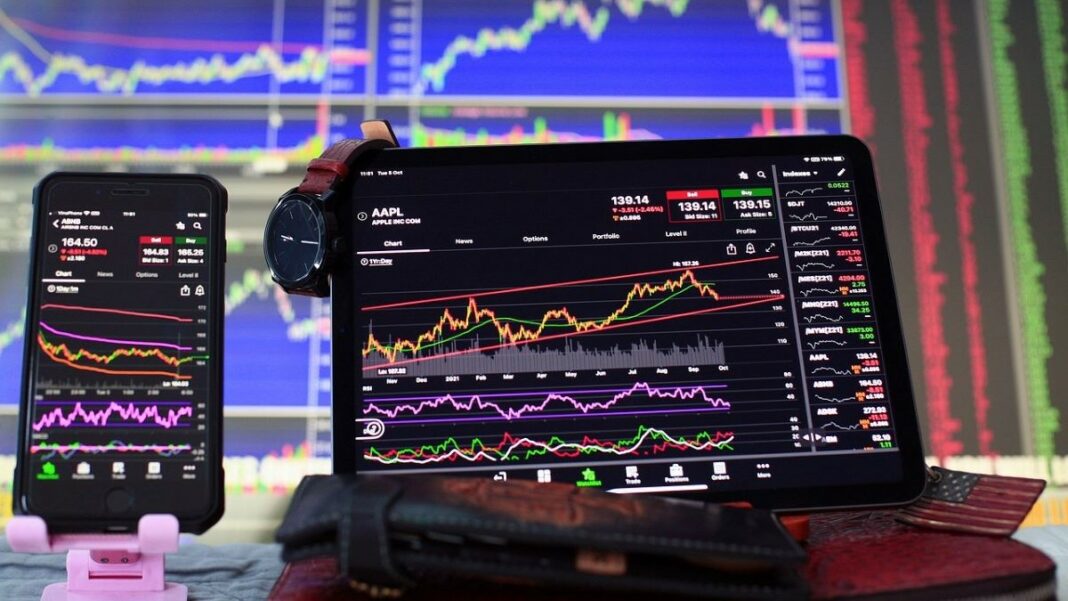 statistical arbitrage represented by stock market charts on a phone. a laptop, and a large PC monitor